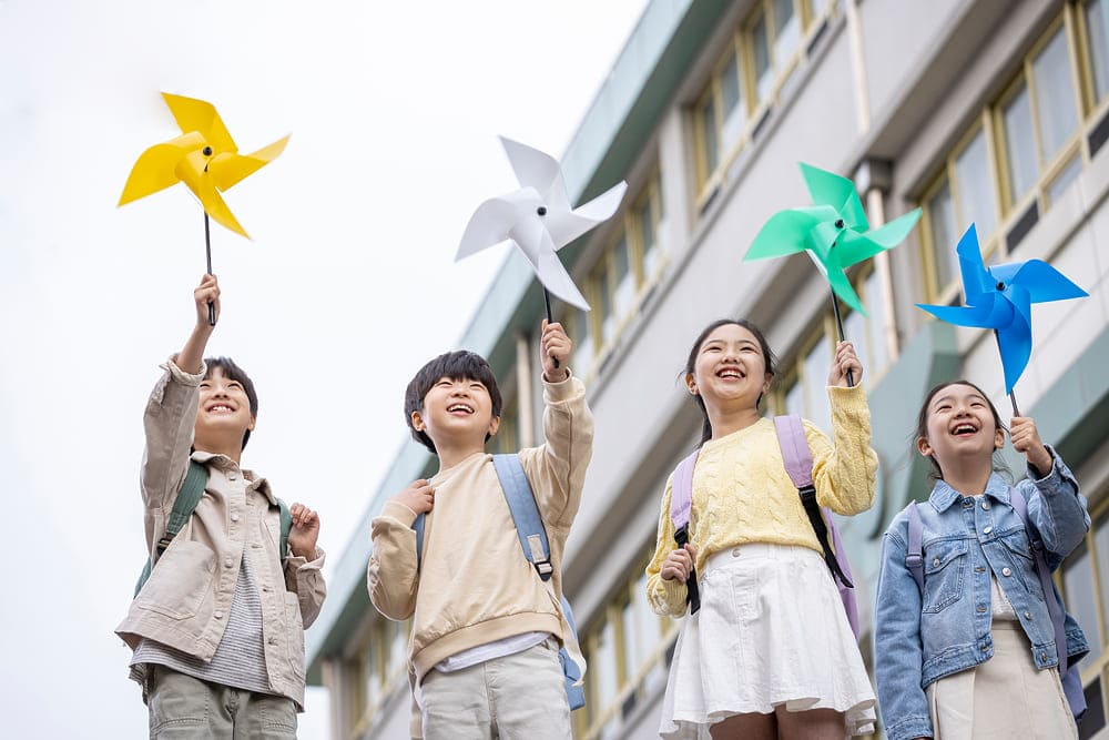 Anak-anak ceria memegang kincir warna-warni, menikmati hari penuh kebahagiaan di sekolah.